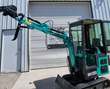 Teal MH13RX mini excavator with boom extended, toothed bucket and thumb raised, enclosed cab and rubber tracks