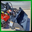 Gray 4-in-1 bucket mounted on a red mini skid steer, clamp jaw open with coiled hydraulic hoses