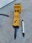 SB45 hydraulic breaker viewed down its length, moil chisel fitted and a spare chrome chisel alongside