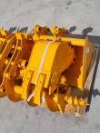 Yellow excavator bucket with twin pin lugs on the pallet, ripper shanks and auger bit alongside