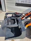Gray flat-bottom grapple bucket on an orange mini skid steer, top view of the shell, grapple arm and hoses