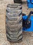 Rough-terrain lug tire on a blue Genie boom lift chassis, hydraulic hoses at the axle