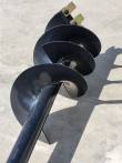 Auger bit's black steel flighting spiraling up the shaft to the gold two-bolt mounting tabs