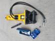 Yellow breaker from the bracket end: black top-mount bracket and pin, coiled hoses, chisel and tool boxes