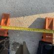 Two orange bolt-on grapple teeth with a tape measure showing about 10 inches of tine spacing between them