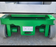 Green vertical mast lift base up close: solid non-marking tires, drive wheels and load decal under the platform