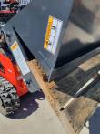4-in-1 bucket's serrated clamshell jaw gripping a wooden pallet board, falling-blade warning decal on the shell