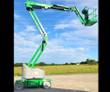 Green articulating boom lift, boom raised and reaching out sideways with the empty work platform at the end