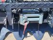 Forestry winch drum wound with steel cable, roller fairlead with hook and red strap under a diamond-plate guard