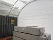 White back wall with four vent openings inside a container shelter, stacked sheet goods in front