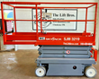 Red Skyjack SJIII S3219 electric scissor lift, lowered, side view with roll-out extension deck