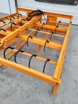 Hay accumulator grapple frame, rows of curved steel bale hooks with hydraulic hoses and a red quick coupler