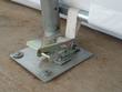 Ratchet tensioner and strap anchoring the fabric cover to a galvanized base plate bolted to concrete