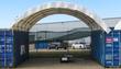 White container shelter forming an open-ended bay between two blue shipping containers
