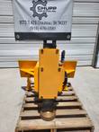 Yellow hydraulic post driver standing on a pallet, quick-attach mount and domed driver head at the base