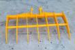 Yellow excavator rake seen from above, seven curved tines and twin pin-boss mounts on the frame