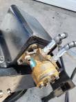 Rust-tinged hydraulic drive motor bolted to the compaction wheel's black frame, steel hose fittings