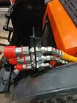 Auxiliary coupler bracket with three flat-face quick connects and red caps, plumbed on a mini skid steer
