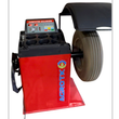 Red computer wheel balancer with a gray ribbed tire on the shaft, digital readouts lit, hood raised