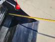 Tape measure across the black 4-in-1 bucket's depth, reading about 23 inches, red-capped coupler above