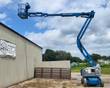 Genie Z-40/23N articulating boom lift, boom raised and reaching out over a metal building