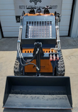 QB-480 mini skid steer head-on: dirt bucket on the quick-attach, red hydraulic couplers and rubber tracks