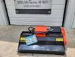 Black flail mower with orange drive cover and spec tag, below the shop address banner
