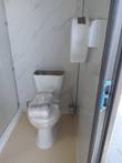 Portable restroom interior: plastic-wrapped white toilet, marble-look wall panels, wall-mounted dispenser and bin