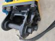 Breaker's black top-mount bracket bolted to the yellow housing, mounting pin and hydraulic hose alongside