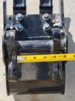 Tape measure across the trenching bucket's bolted hitch and pin bosses, past the four-inch mark