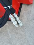 Two hydraulic hoses ending in steel quick-connect couplers, zip-tied against the red rake frame