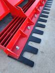 Black toothed leveling bar bolted along the red rake frame, welded ribs and gussets behind the teeth