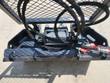 Forestry winch in its frame: cable drum, hydraulic motor, hoses and red-capped couplers under a mesh deck