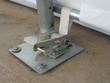 Fabric building base plate bolted to concrete: galvanized foot, frame leg and ratchet tensioner on the cover strap