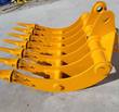 Yellow excavator rake angled to show its curved tine arms, replaceable teeth and pin ears