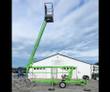 Green Nifty TM34 towable boom lift with the boom raised and work platform elevated on outriggers