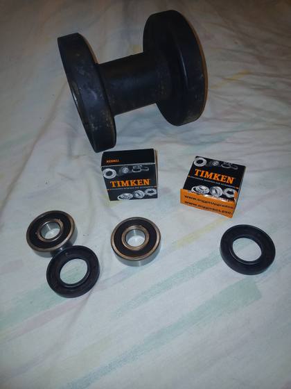 Two Timken bearings and two black oil seals beside a bottom track roller from a mini skid steer