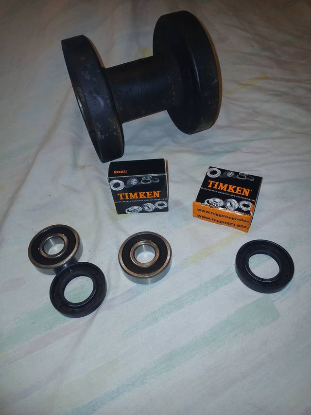 Two Timken bearings and two black oil seals beside a bottom track roller from a mini skid steer