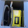 AGROTK 680 post driver storage bay: spring-wrapped hydraulic hoses coiled beside a yellow tool box