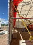 Red and white dual truss fabric building being erected, boom lift positioned inside for install