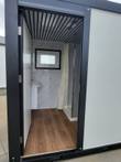 Portable restroom interior through open door: vanity sink, hinged window, marble-look walls and shower stall
