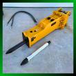Yellow SB45 hydraulic breaker at an angle, black moil chisel fitted, spare chrome chisel and two hydraulic hoses