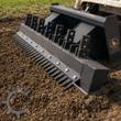 Wolverine ripper bar mounted on a skid steer, tines tearing through broken-up soil