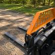Wolverine 48-inch pallet forks mounted on a mini skid steer's quick-attach plate, orange backrest above black tines