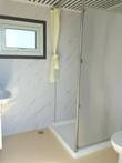 Bastone portable bathroom interior: shower stall with curtain, marble-look wall panels, corner sink, toilet