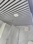 Striped panel ceiling with round recessed light and wall vent fan above the shower stall