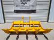 Yellow TOFT10R excavator rake front-on, five tine tips over a serrated bar, cross tubes and twin lugs