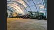 Inside a fabric storage building: a camper truck, pickup, skid steer and reach forklift