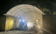 Skid steer and mini excavator under a container shelter at night, back wall enclosing the far end