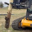 Tree and post puller on a JCB track loader, gripping a muddy wooden fence post pulled out of the ground